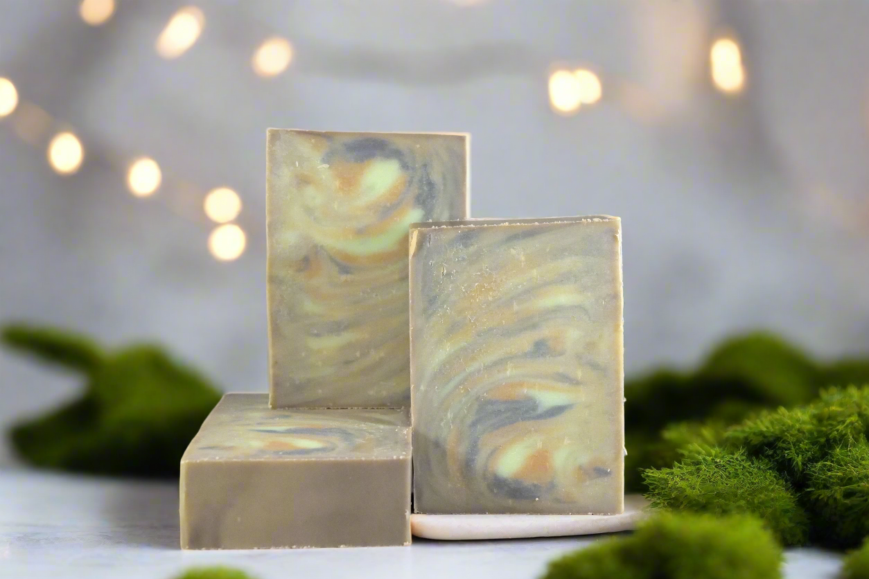 Three bar soaps on a platform with a decorative background featuring green moss and small lights, reflecting a natural and serene atmosphere.